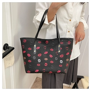 Detail of black tote bag with red lip prints, long shoulder strap, and gold rivet accents