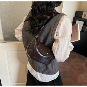 Detail of dark brown glossy leather shoulder bag with vintage metal rivets on the side