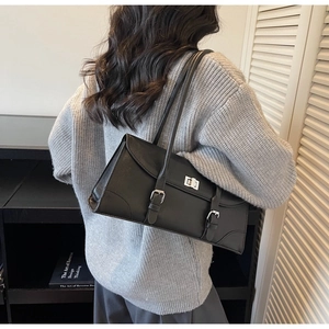 Detail of black matte leather shoulder bag with silver turn-lock and adjustable buckle straps
