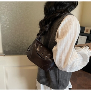 Detail of dark brown glossy patent leather saddle bag with vintage metal rivets decor