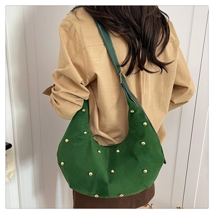 Detalle del bolso hobo de ante verde oscuro con tachuelas doradas en la modelo
