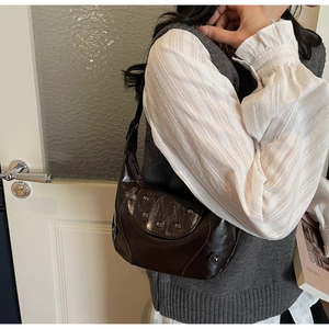 Detail of dark brown patent leather hobo bag with round metallic rivets on shoulder strap