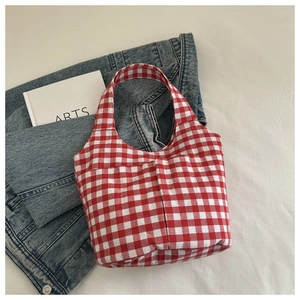 Detail view of the red and white checkered canvas bucket bag on denim and decorative book