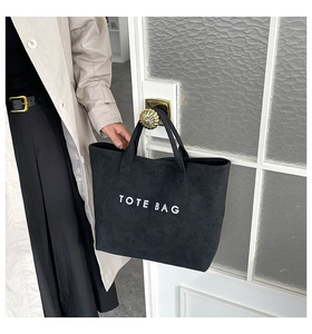 Detail einer schwarzen Wildleder-Einkaufstasche mit TOTE BAG Aufdruck an einer Tür