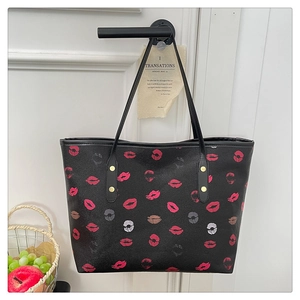 Detail of a black tote bag with red and pink lip prints hanging on a white door handle