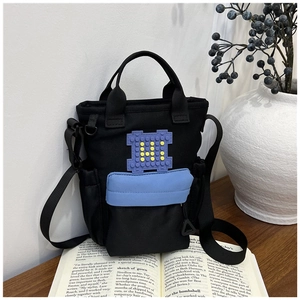 Close-up of black canvas crossbody bag with blue zipper pocket and colorful patch decor