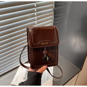 Detail view of small brown faux leather shoulder bag with gold metal pendant and strap