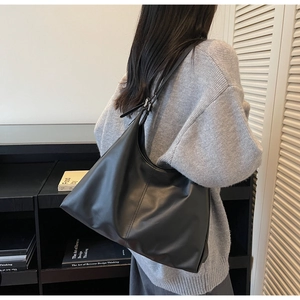 Detail of a black leather hobo tote bag with adjustable strap on a woman in grey sweater