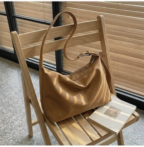 Detailed macro view of brown vintage leather tote bag with wide strap on a wooden chair