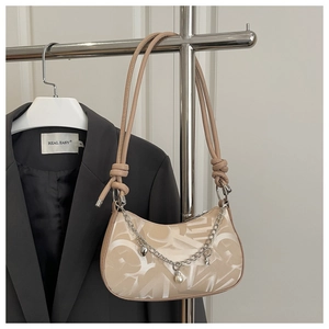 Detail of a chic beige underarm bag with abstract letters and decorative silver chain charms