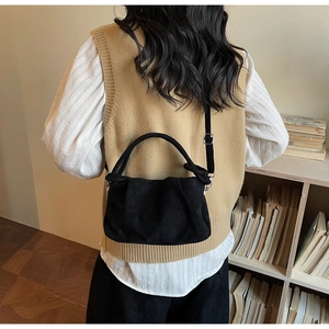 Detail of minimalist black pleated suede bag worn crossbody in a warm interior setting