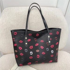 Fashionable black faux leather tote bag with red and pink lip prints and gold rivet details