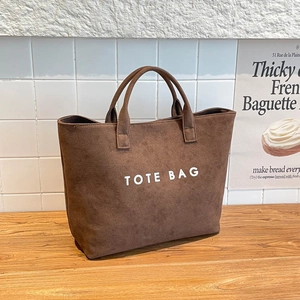 Braune Wildleder-Einkaufstasche mit TOTE BAG-Schriftzug in stilvollem Lifestyle-Ambiente