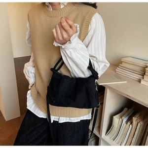 Detail of black pleated suede crossbody bag worn by model in a cozy indoor setting