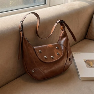 Vintage dark brown saddle bag with silver studs on a beige sofa, stylish lifestyle view