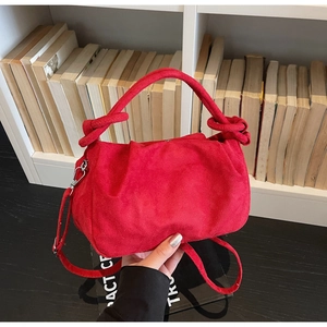 Close-up of red suede cloud bag featuring knotted handle and detachable shoulder strap