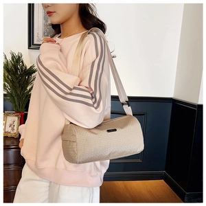 Close-up of beige woven texture sports barrel bag with adjustable strap on a shoulder