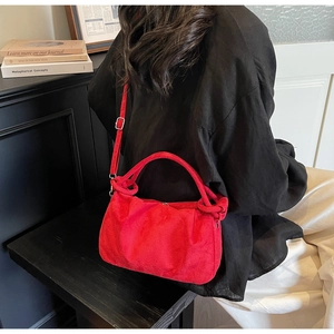 Detail view of red suede pleated cloud bag with textured handle and adjustable strap