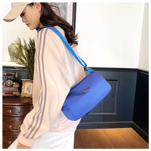 Detail view of blue checkered cylinder crossbody bag with metallic logo on textured nylon