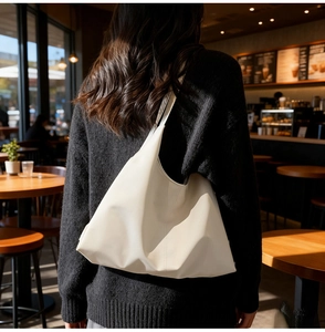Minimalist beige oversized tote bag in soft leather texture worn by a model in a cafe