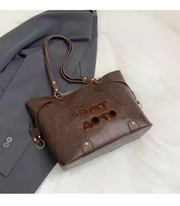 Close-up of vintage brown tote bag with plush textured DNT AOTO lettering and gold rivets
