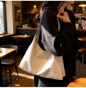 Lifestyle view of large white leather tote bag worn by a model in a sunlit cafe