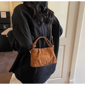Detail of brown suede cloud bag with pleated texture and adjustable strap in lifestyle setting