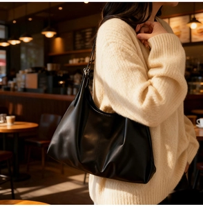 Close-up of a large black soft leather tote bag worn over the shoulder in a cafe