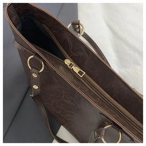 Detail of dark brown tote bag showing textured leather, gold zipper and interior pocket