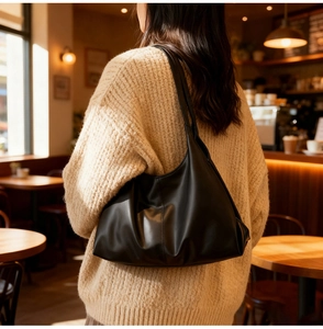 Minimalist black PU leather tote bag shown on model in a cozy cafe setting