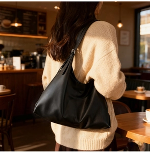 Detail of a large black leather tote bag worn by a model in a cozy cafe setting