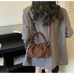 Detailed view of dark brown pleated suede cloud bag with cylindrical handle and strap