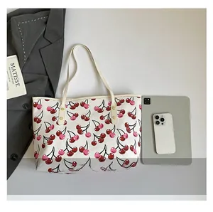 Flat lay of off-white tote bag with cherry print next to magazines and accessories