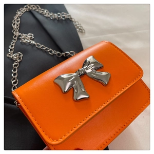 Détail de mini sac bandoulière orange avec nœud argenté et bandoulière en chaîne métal