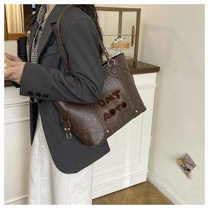 Detail of vintage brown textured tote bag featuring 3D embroidered logo and metal bottom studs
