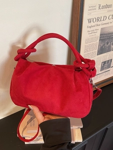 Red textured suede cloud bag with knot handles and crossbody strap in a stylish setting