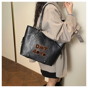 Detail of black textured tote bag featuring DMT AOTO lettering and metal bottom studs
