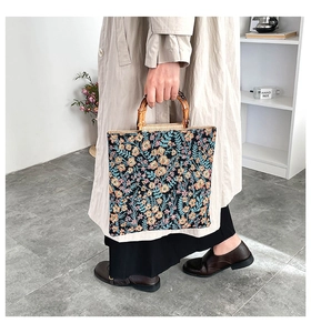 Close-up of floral embroidery texture and natural bamboo ring handles on a black tote bag