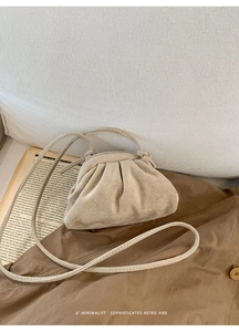 Gedetailleerde macro-opname van beige geplooide cloud-tas op een vintage boek