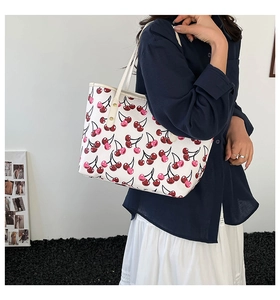 Close-up of white cherry print tote bag with metal rivets and leather texture