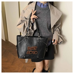Close-up of black PU leather tote bag featuring brown plush DMT AOTO lettering and handles
