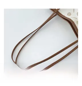 Close-up of brown leather handles with precise stitching on a beige printed tote bag