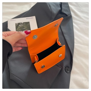 Détail du mini sac à rabat orange vif avec deux boucles magnétiques argentées et texture lisse