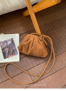 Bruine plooibare wolkentas van imitatie-suède met slanke schouderriem op houten achtergrond