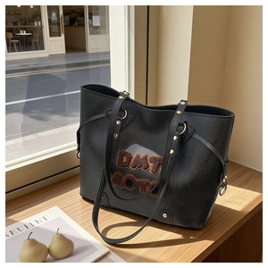 Close-up of black tote bag featuring brown plush embroidery and gold rivet details