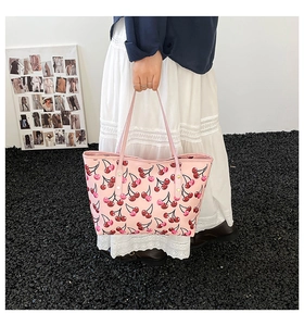 Detail shot of a pink tote bag featuring a vibrant red cherry pattern and golden studs