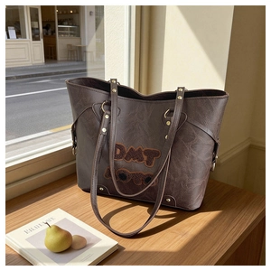 Detail of vintage textured brown tote bag with DMT plush patches and gold studs on a table