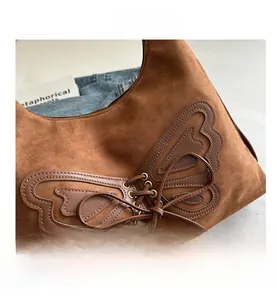 Close-up of brown suede shoulder bag featuring a unique butterfly leather patch and drawstring