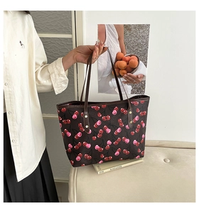 Close-up of large tote bag featuring cherry print and brown leather shoulder straps