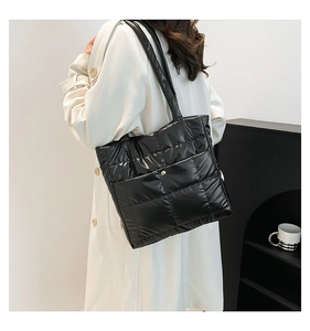 Detail of black quilted puffer tote bag in glossy nylon fabric worn with a beige trench coat